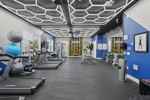 Fitness center at Millennium Apartments with treadmills, exercise balls and a resistance band rack under hexagon LED lighting