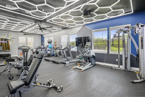 Fitness center at Millennium Apartments with a row of cardio machines and a weight bench under hexagon LED lighting