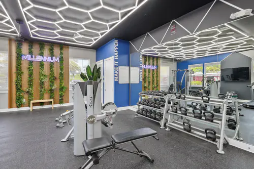 Dumbbell and kettlebell racks beside a living wall with a lit Millennium sign in the fitness center